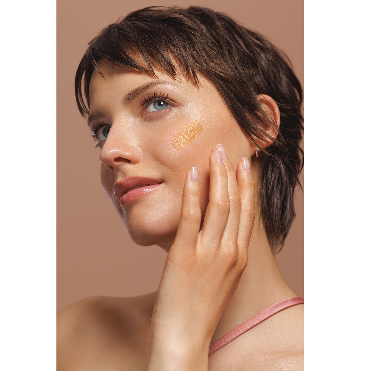 Womans Facde applying the Weleda Sun-kissed Bronzing Serum Booster Drops on a white background