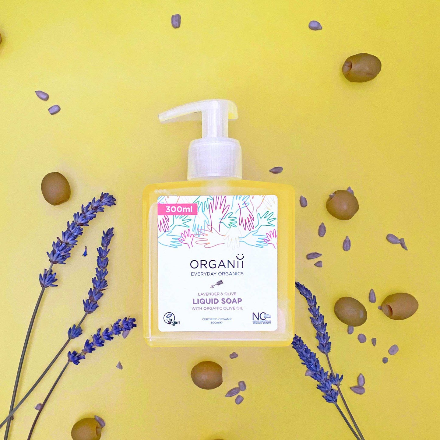 Organii Lavender and Olive Liquid Soap in a clear square bottle with a pump on yellow background with olives and lavender