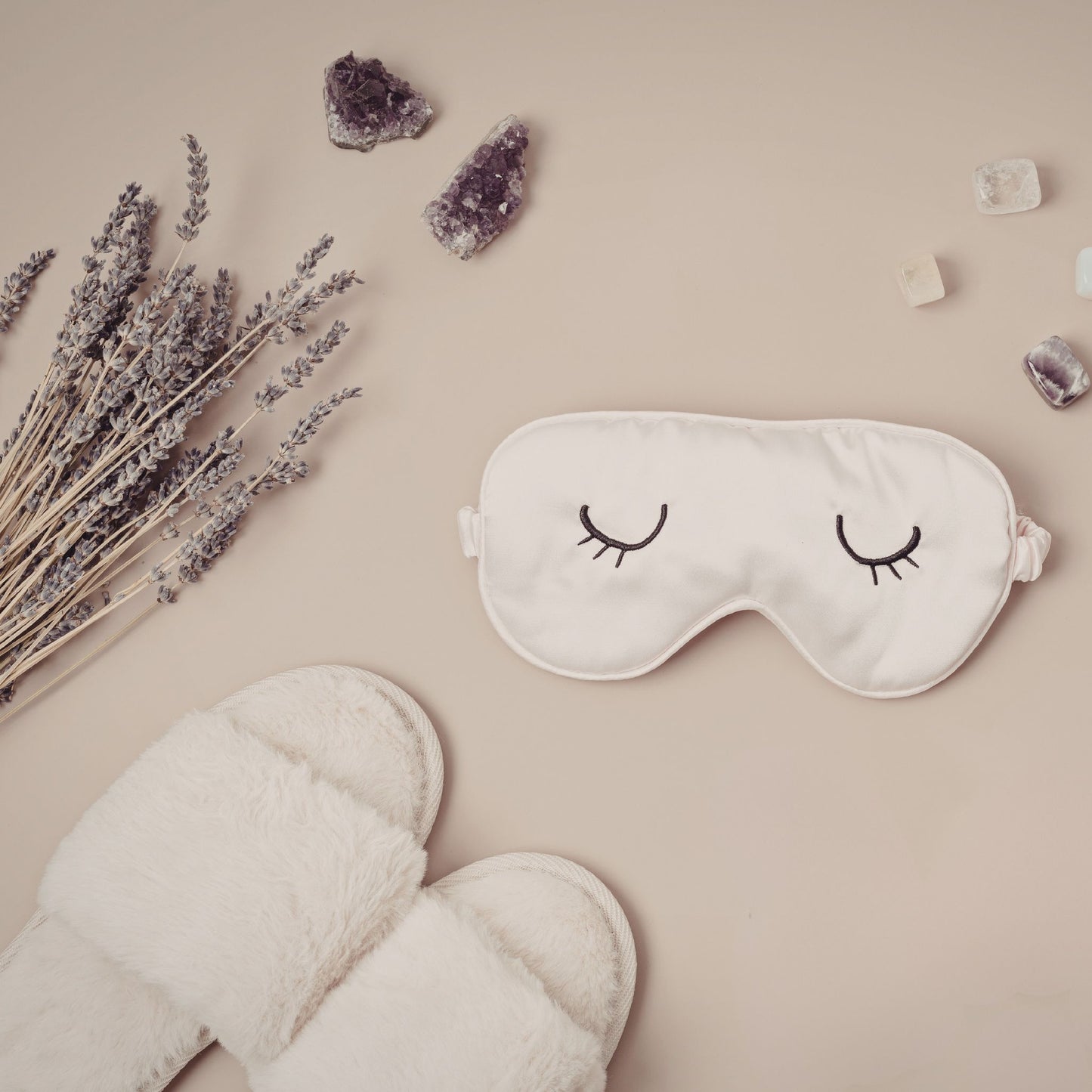 Sleep mask with eye design, lavender, and slippers on a beige background