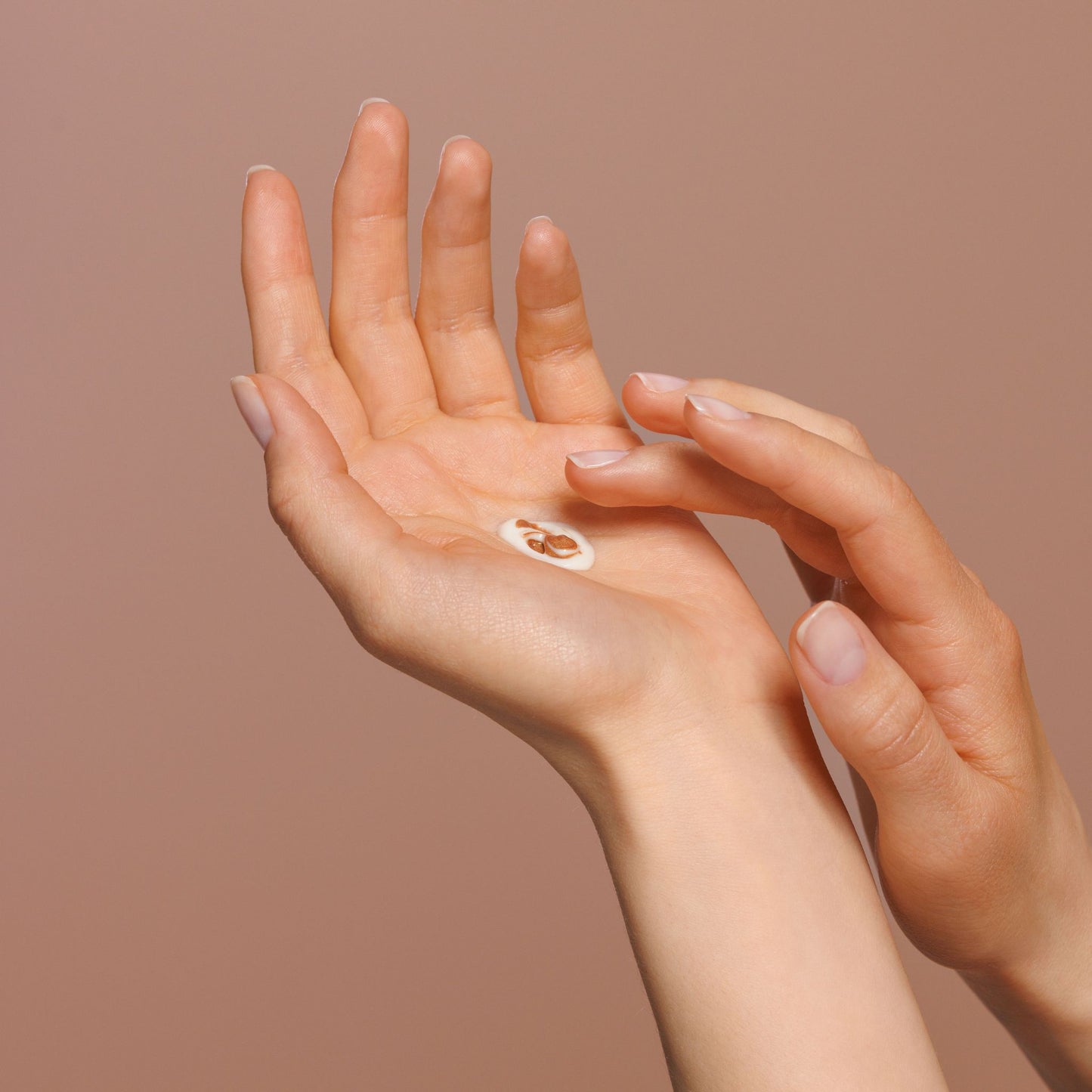 Two hands against a solid warm beige background, with a small oval white patch containing a brown patch applied to the left hand.