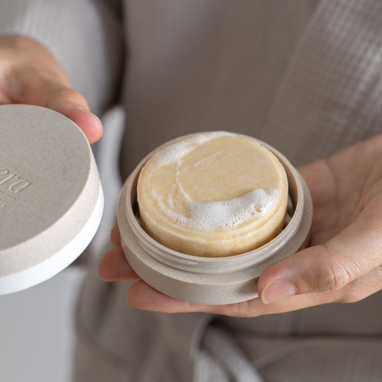 Hands holding a lavera natural shampoo bar in a sustainable beige travel case with soapy foam.