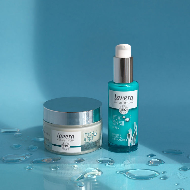 Lavera Hydro Refresh skincare duo, featuring the Cream-Gel and Serum, displayed on a cool blue surface accented by clear, glistening water droplets.