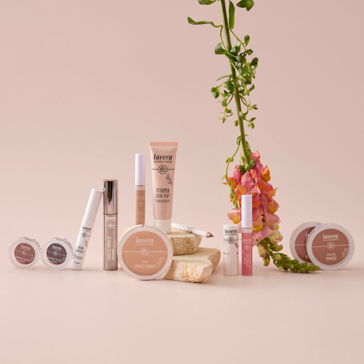 Lavera Make Up Colour Cosmetics collection of eyeshadow, foundation, face powder, mascara, lipgloss and lipstick on pink background 