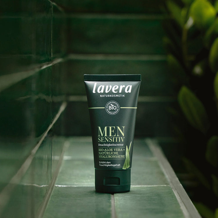 A tube of Lavera Men Sensitive (moisturising cream) with organic aloe vera and natural hyaluronic acid, displayed on a dark green tiled ledge.