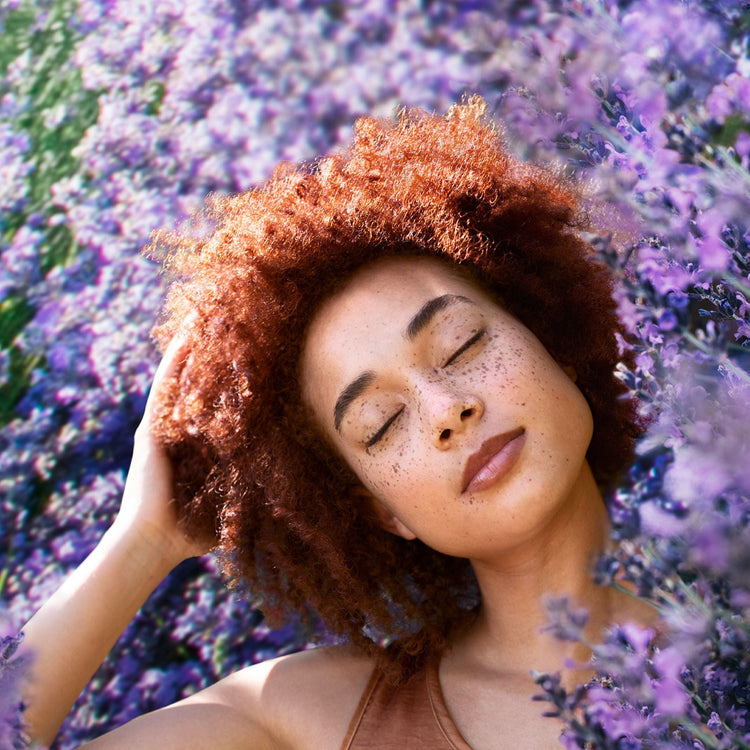 Person with eyes closed and a peaceful expression, leaning their head back into a field of vibrant purple lavender.