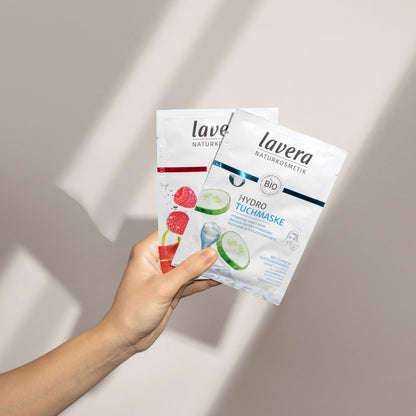 Hand holding two Lavera Hydro Sheet Face Mask on a white background.