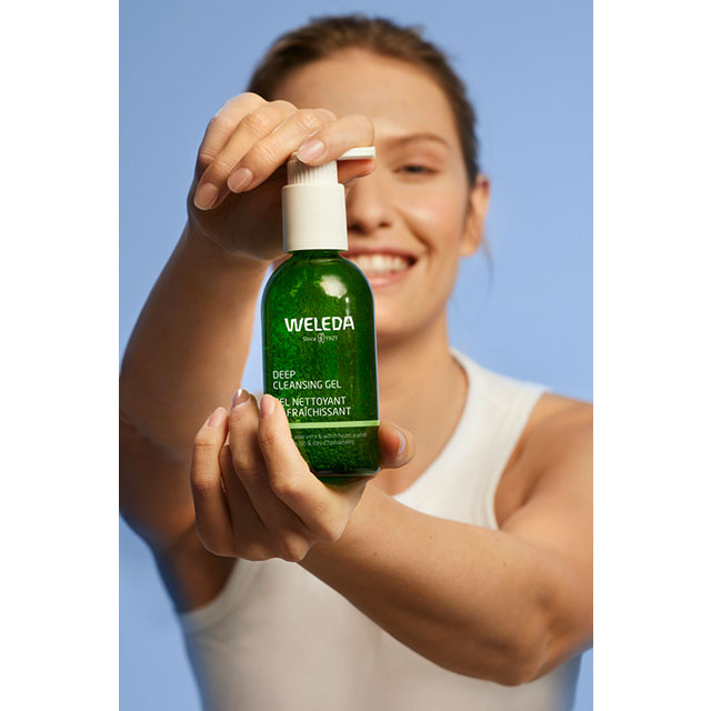 Woman holding Weleda Deep Cleansing Gel with organic aloe vera and organic witch hazel in a green glass bottle
