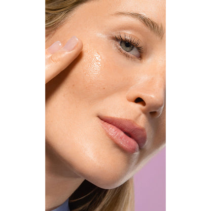 Close-up of a womans face showing the serum on her cheek on a white background