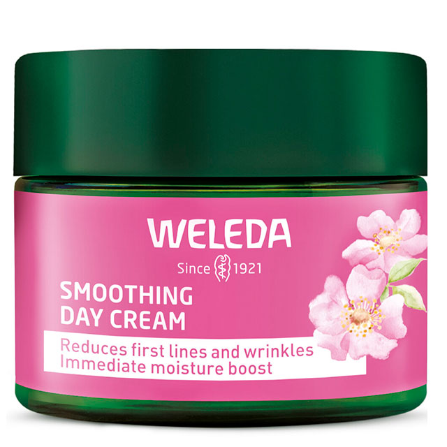 Weleda smoothing day cream is in a green jar with pink label with pink flowers and green lid on a white background