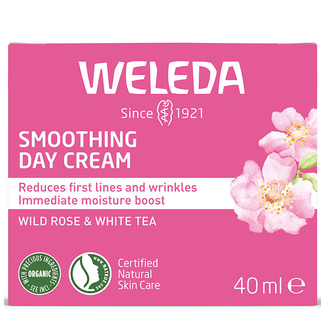 Weleda Smoothing Day Cream with wild rose and white tea is in a ink and white cardboard box with light pink flowers on a hite background