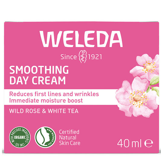 Weleda Smoothing Day Cream with wild rose and white tea is in a ink and white cardboard box with light pink flowers on a hite background