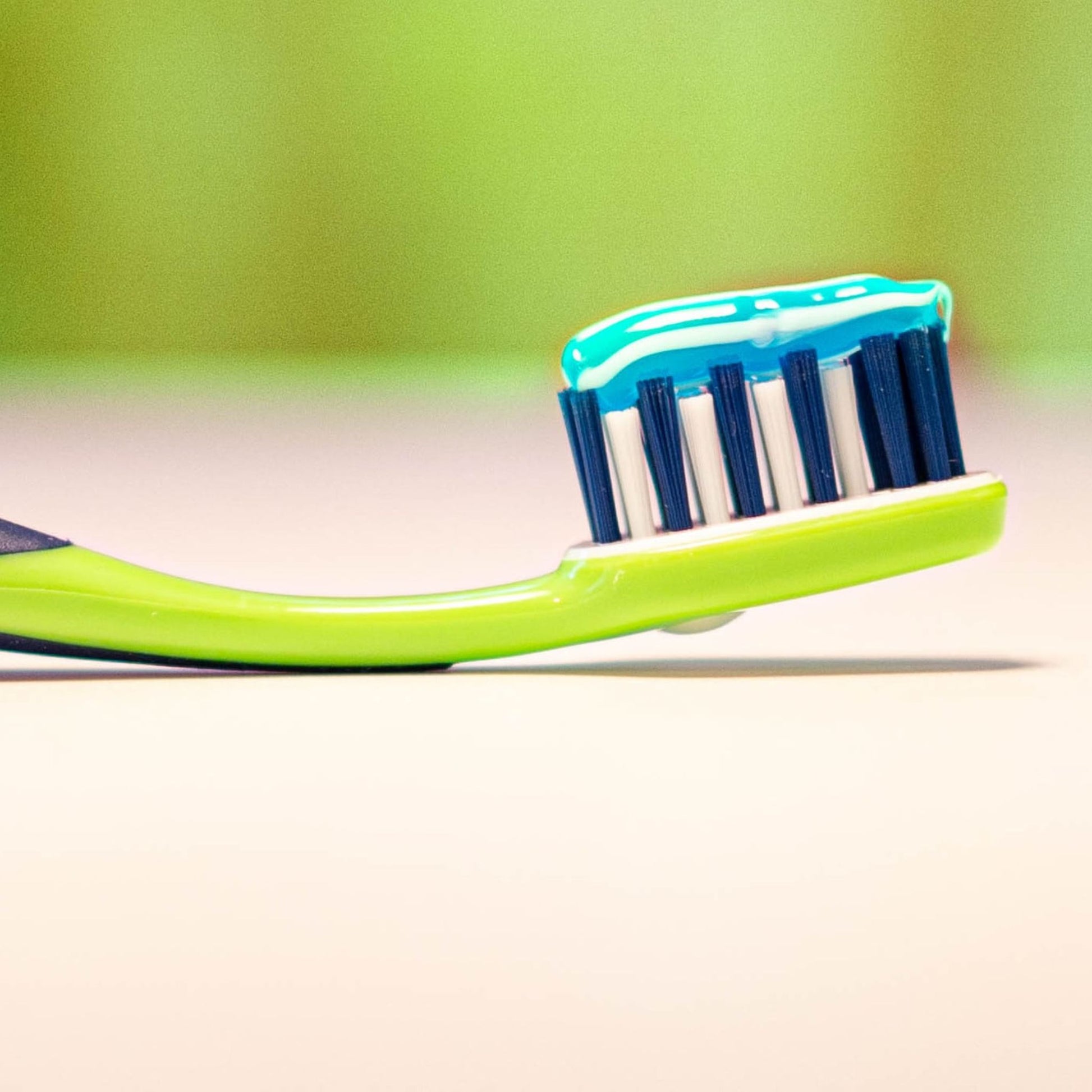 Green toothbrush with blue and white toothpaste on a blurred green background