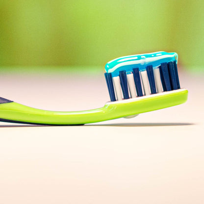 Green toothbrush with blue and white toothpaste on a blurred green background