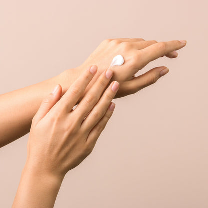 Two hands applying cream on a beige background
