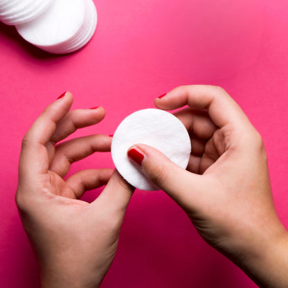 Hands holding a white cotton pad against a pink background