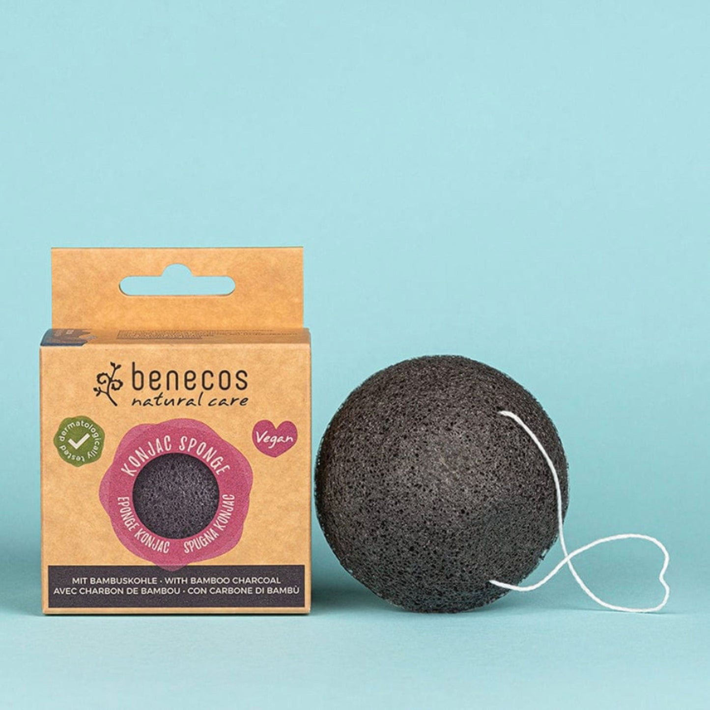 A Benecos natural care Konjac Spongie (bamboo charcoal sponge) shown next to its brown cardboard packaging box on a solid light blue background.