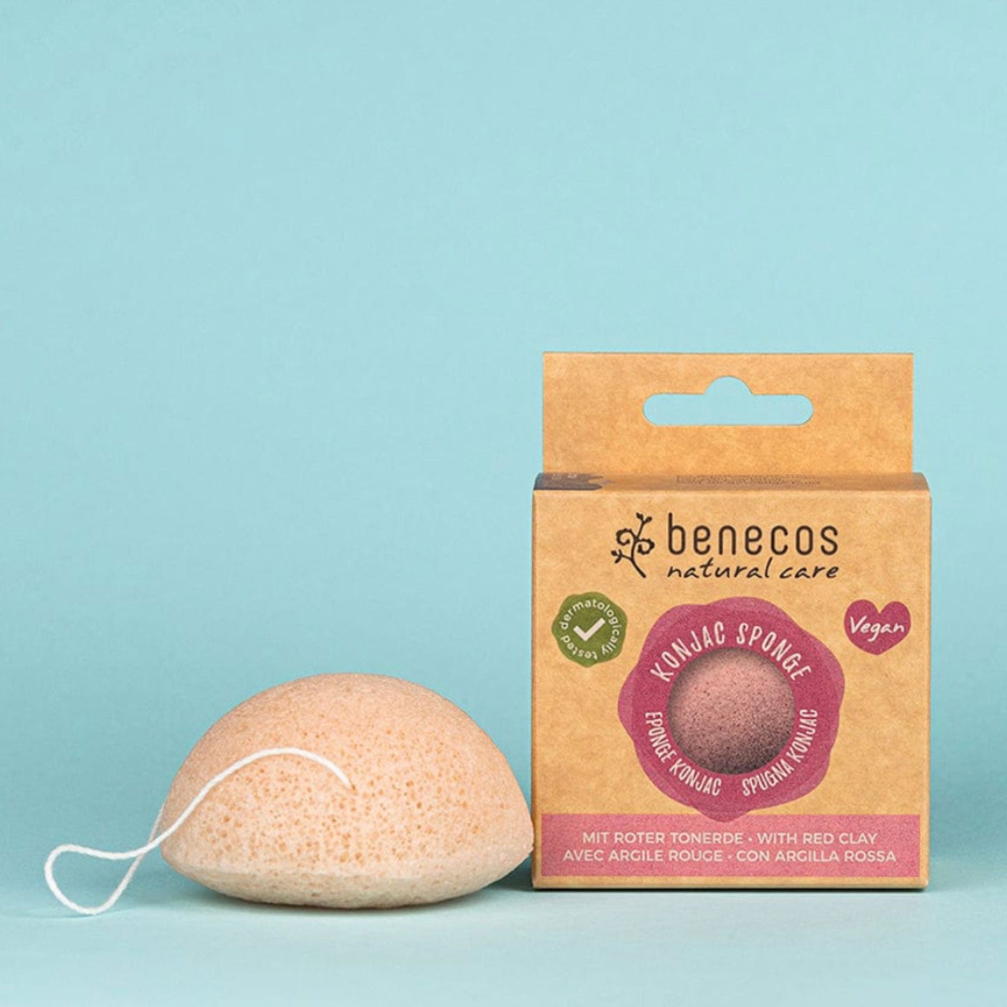A Benecos Natural Care Xoniac Sponge exfoliating sponge next to its kraft paper packaging box, set against a solid light blue background.
