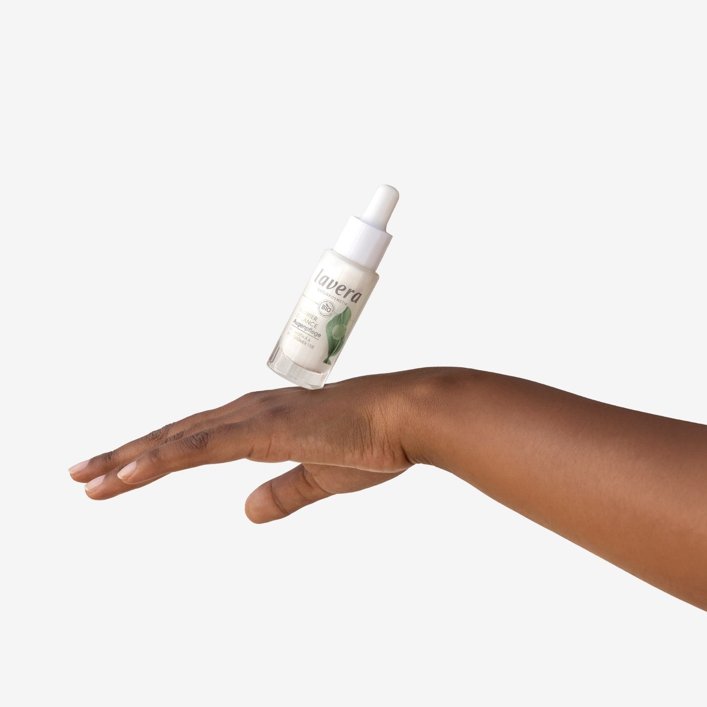 Lavera Barrier balance eye cream in clear glass dropper bottle with a white dropper cap on a back of hand on a white background.