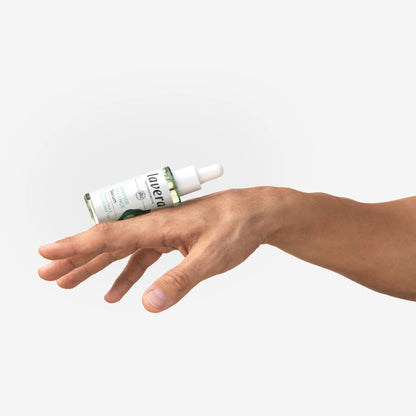 A hand holding a small dropper bottle with a white label and green accents against a light gray background.
