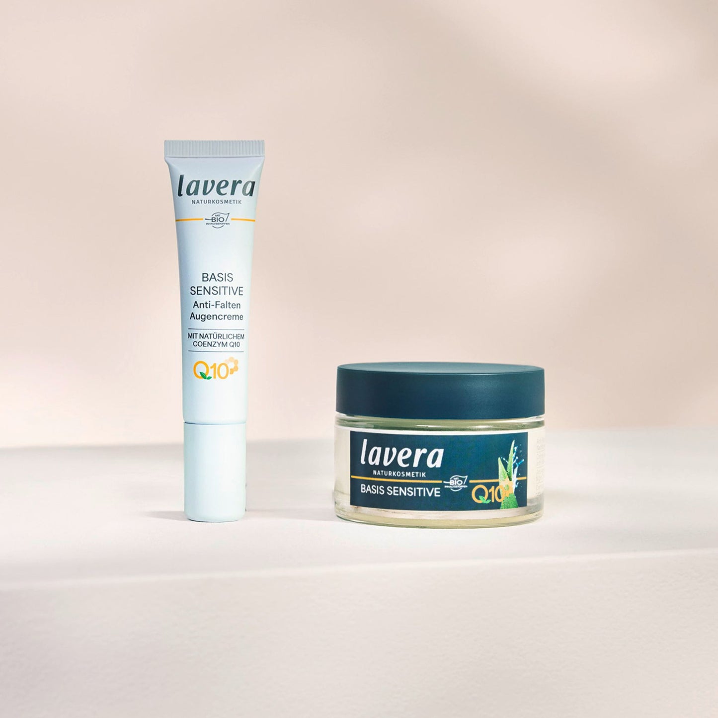 Lavera Basis Sensitive Anti-Aging Cream  in a white squeeze tube and a clear jar with a dark teal lid Lavera Basis Sensitive night cream, set against a soft beige background.