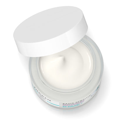 An open round cosmetic jar with a white lid leaning against the container, showing a smooth off-white cream product inside. The jar has a clear lower section and a white label with small blue text, photographed on a clean white background.