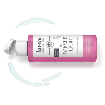 A pink bottle of Lavera Organic Soft Eye Make-Up Remover with a white cap, shown on a white background with decorative light blue makeup smears.