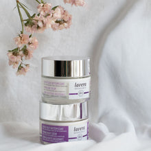 Two jars of Lavera Face Cream stacked on a white fabric background with soft pink flowers at the top left.