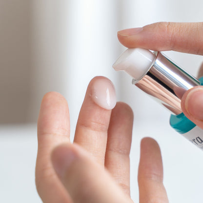 A close-up of a person applying a glossy, translucent lavera hydro refresh serum from a pump bottle onto their finger.