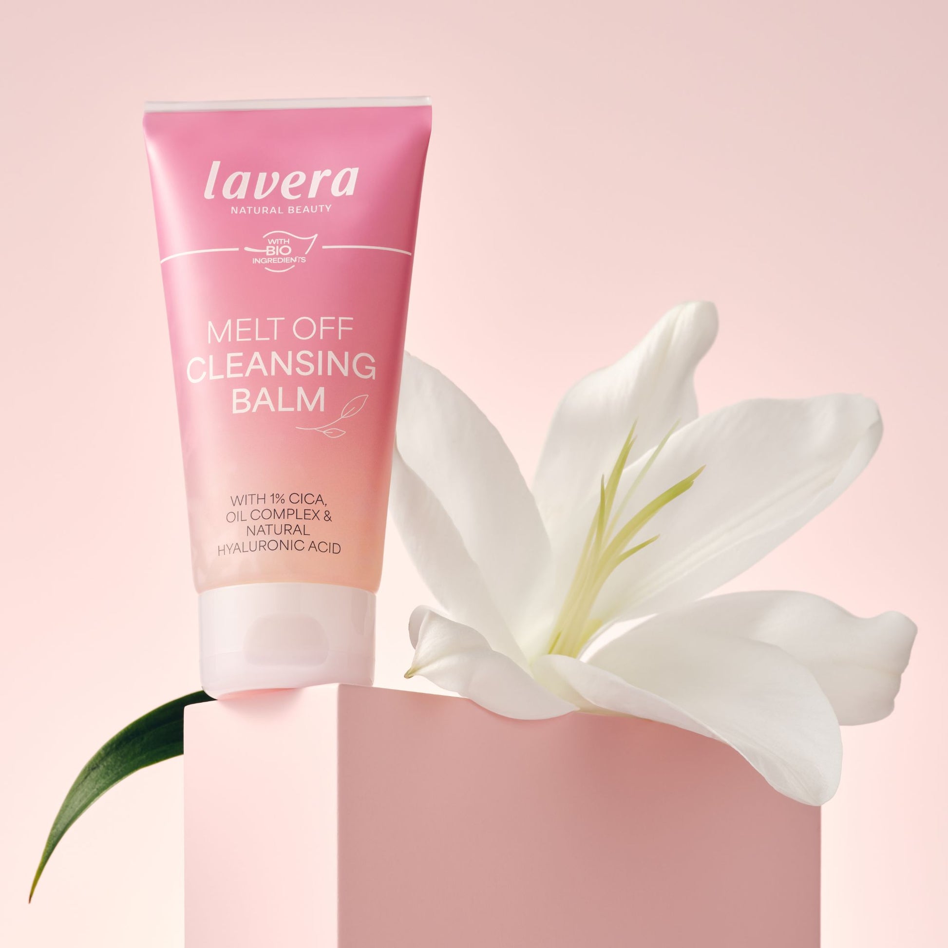 A tub of Lavera Melt Off Cleansing Balm sitting upright on a pink background with white flower