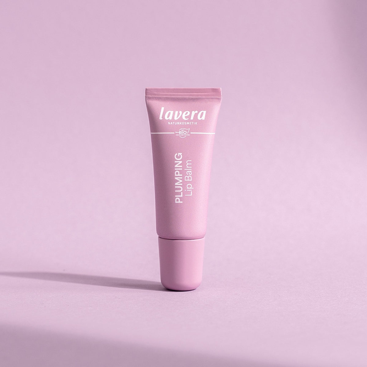 Lavera Plumping Lip Balm in a pink tube, presented on a pink background.