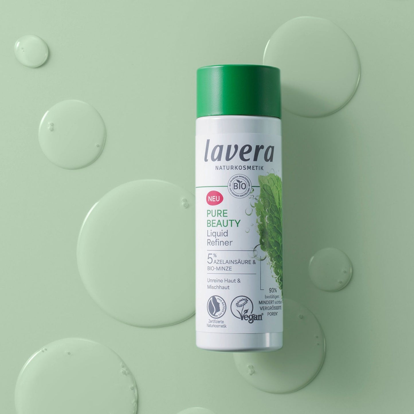 A bottle of Lavera Pure Beauty Liquid Refiner, featuring a white bottle with a dark green cap on a green background