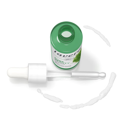A green bottle of lavera Pure Beauty Serum with a white dropper pipette, shown on a white background with decorative droplets.