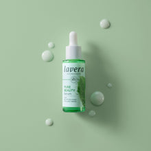 Lavera Pure Beauty Serum in a clear dropper bottle with green liquid, displayed on a light green background with decorative droplet props.