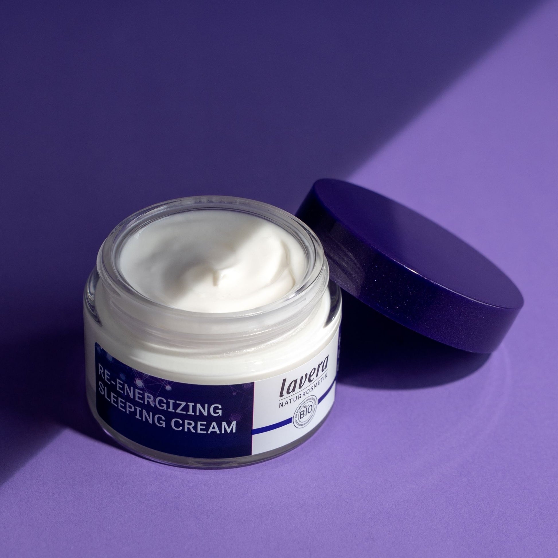 Lavera Re-Energising Sleeping Cream jar open with white text and glowing network graphics, shown on a purple background.