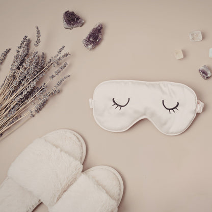 Sleep mask with eye design, lavender, and slippers on a beige background