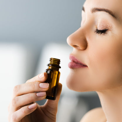 Woman holding a small brown bottle close to her face, possibly an essential oil dropper.
