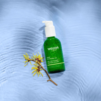 A green bottle of Weleda Deep Cleansing Gel with a white pump dispenser, set against a light blue background with a yellow flower.