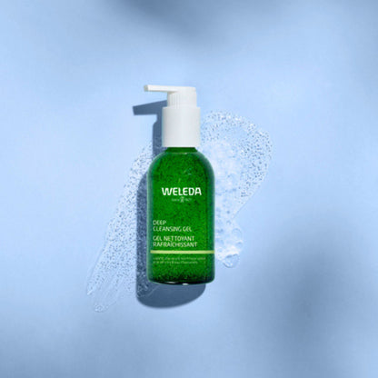 A green bottle of Weleda Deep Cleansing Gel with a white pump dispenser, set against a light blue background with a splash of clear foam around it.