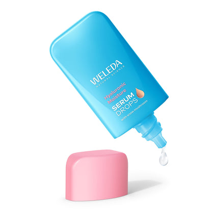 A blue bottle of Weleda Hyaluionic Moisture Serum Drops and pink cap, with a single clear liquid drop falling from the nozzle on a white background.