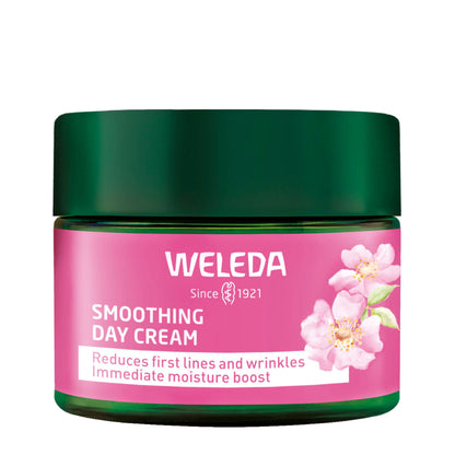 A jar of Weleda Smoothing Day Cream with a dark green lid and a pink label decorated with pink flowers, set against a plain white background.