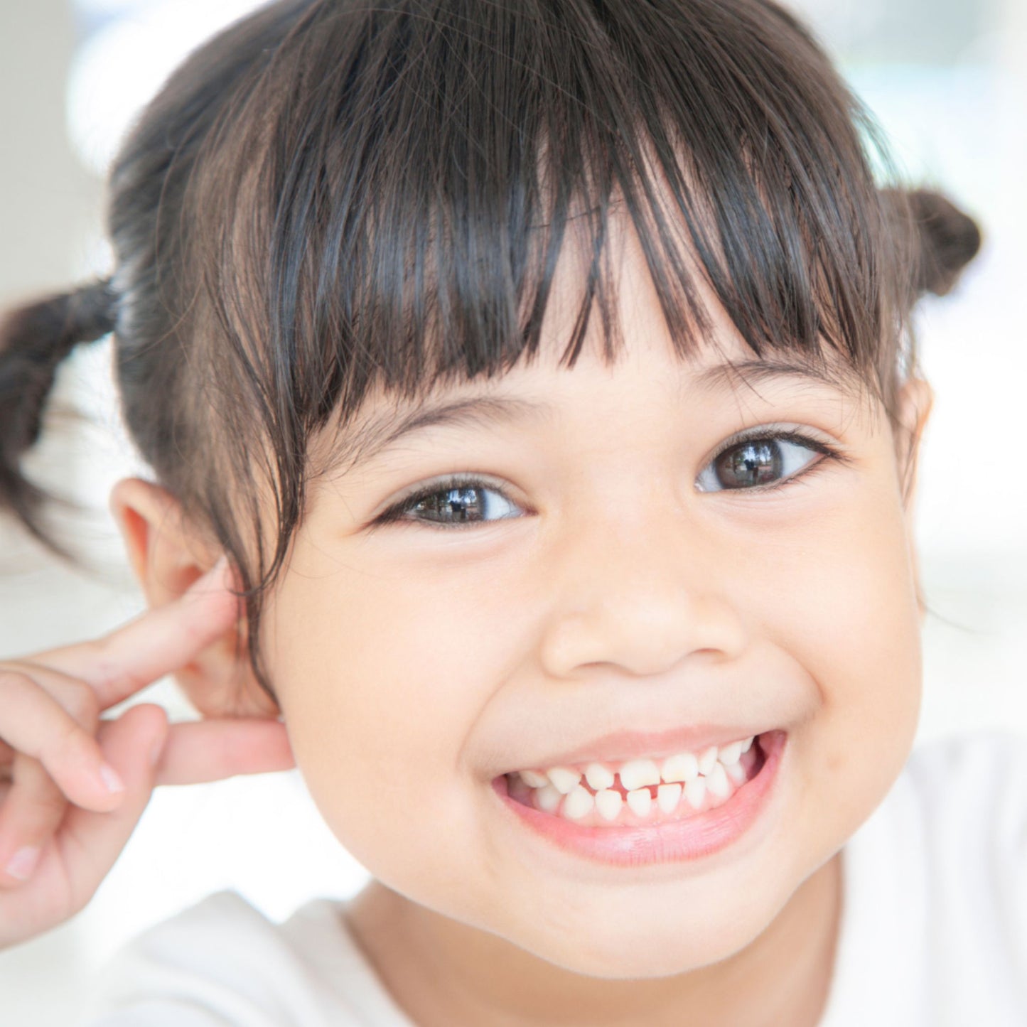 Young girl with pigtails smiling and holding her hand to her ear.